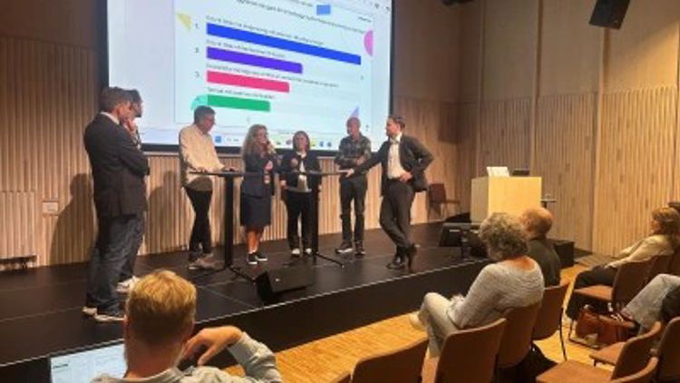 Seks personer står på en scene under en paneldebatt